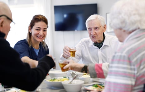Tre äldre och en yngre person äter mat vid ett bord . De skålar med varandra och ser glada ut.