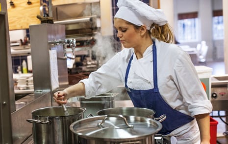 Kock som vispar om i kastrull i ett restaurangkök.