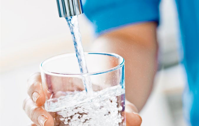 Vatten från kran rinner ner i ett dricksglas