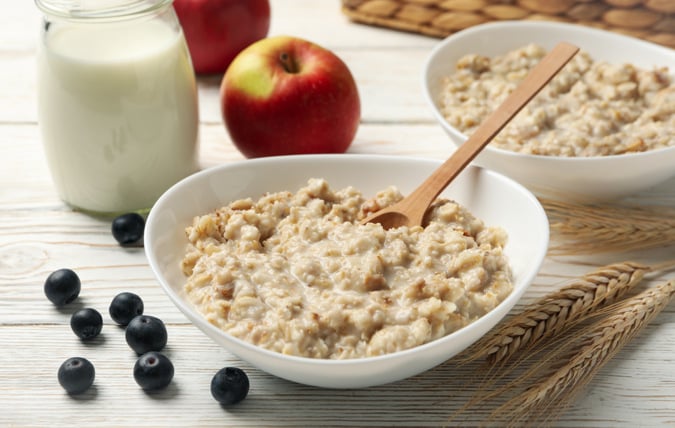 Tallrikar med havregrynsgröt omgivna av blåbär, äpplen och en kanna med mjölk.