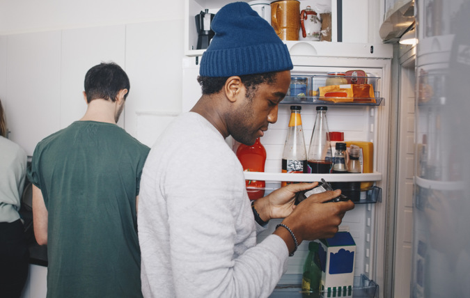 En kille tittar på ett livsmedel framför ett kylskåp.
